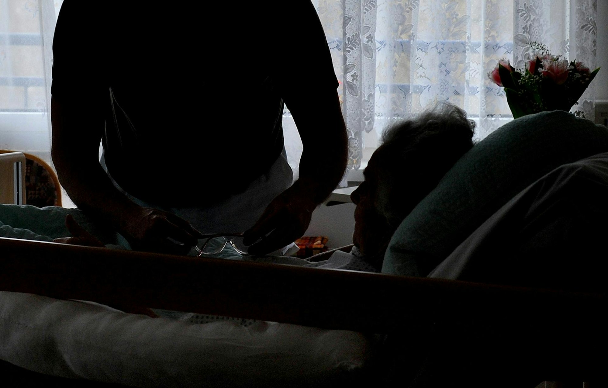 Ein Pfleger hilft einer im Bett liegenden Frau.