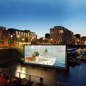Menschen schauen einen Film im Open Air Kino im Kölner Rheinauhaufen
