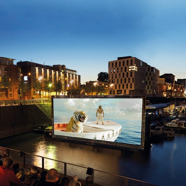 Menschen schauen einen Film im Open Air Kino im Kölner Rheinauhaufen