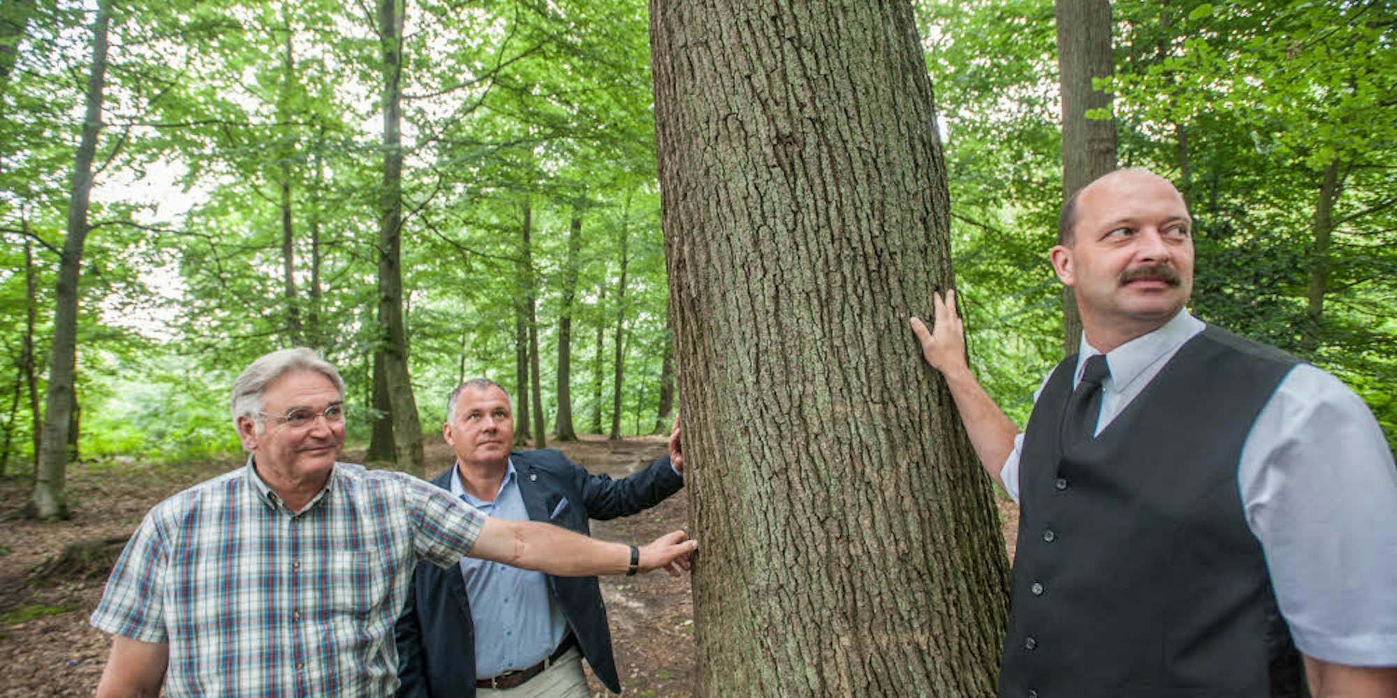 Bestatter Ralf Aschenbroich (von rechts) mit Bürgermeister Frank Steffes und Landwirt Karl-Otto Dickhoven als Beauftragtem des Eigentümers Graf Mirbach von Harff an einem der Bäume des künftigen Friedwaldes im Vorster Busch.