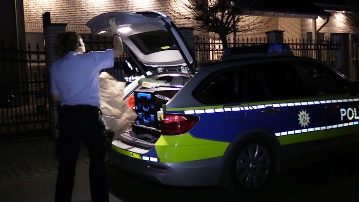 Ein Polizist verlädt eine Papiertüte im Kofferraum eines Polizeiwagens.