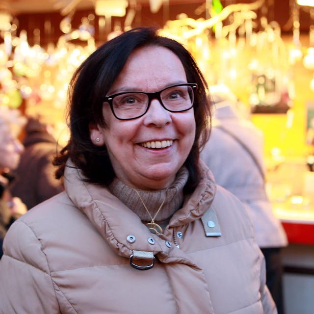 Weihnachtsmarkt-Chefin Monika Flocke steht vor einem erleuchtenden Stand auf dem Weihnachtsmarkt am Köln Dom.