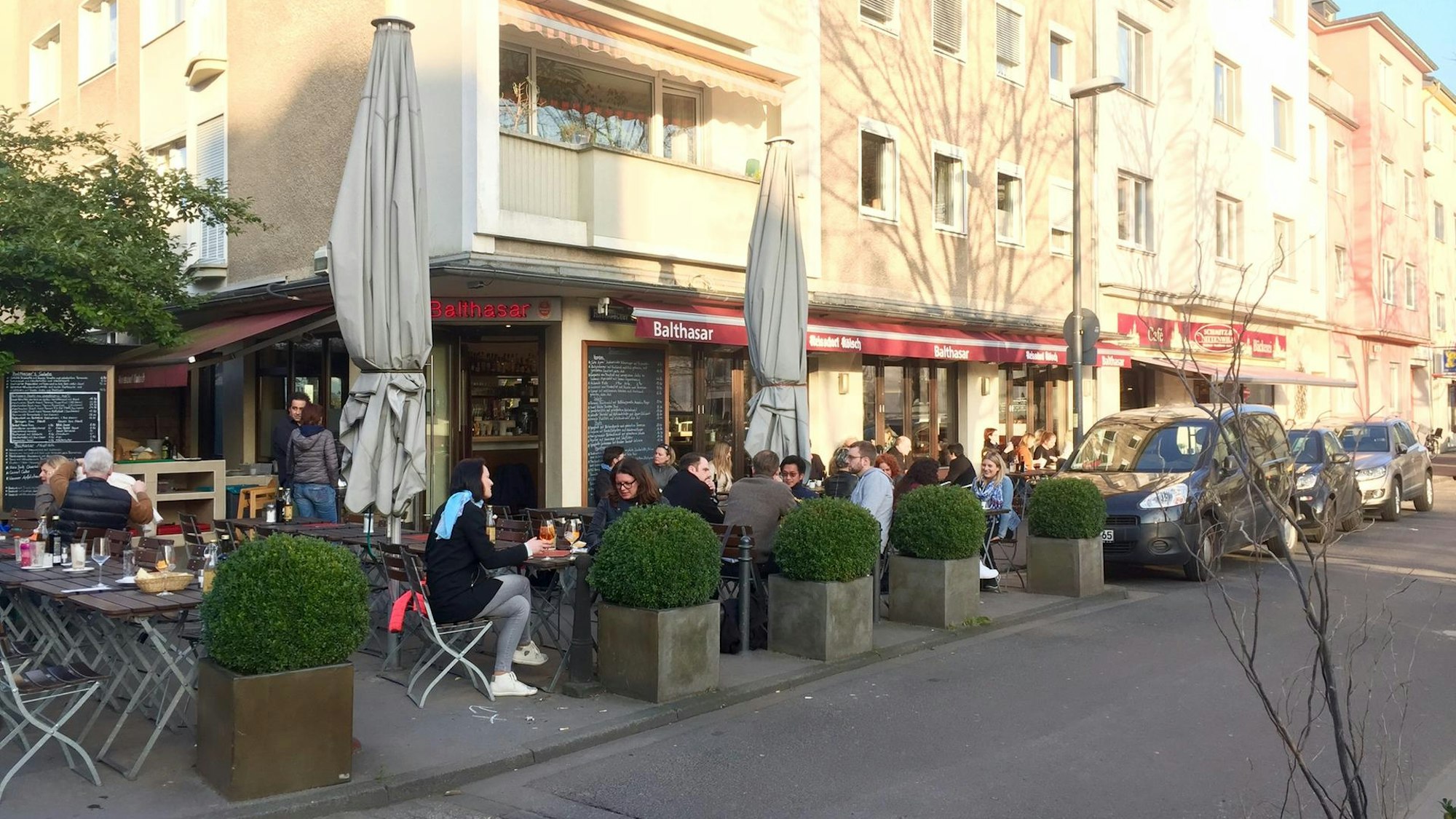 Blick von einer Straße auf Menschen, die draußen vor einem Café sitzen