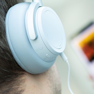 Weißer Over-Ear-Kopfhörer, im Hintergrund unscharf ein Smartphone mit Musikstreamingdienst.
