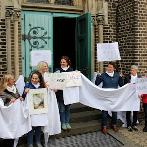 Mit weißen Tüchern und Plakaten demonstrierten Frauen der KFD vor der Kirchenpforte St. Cornelius in Geyen.