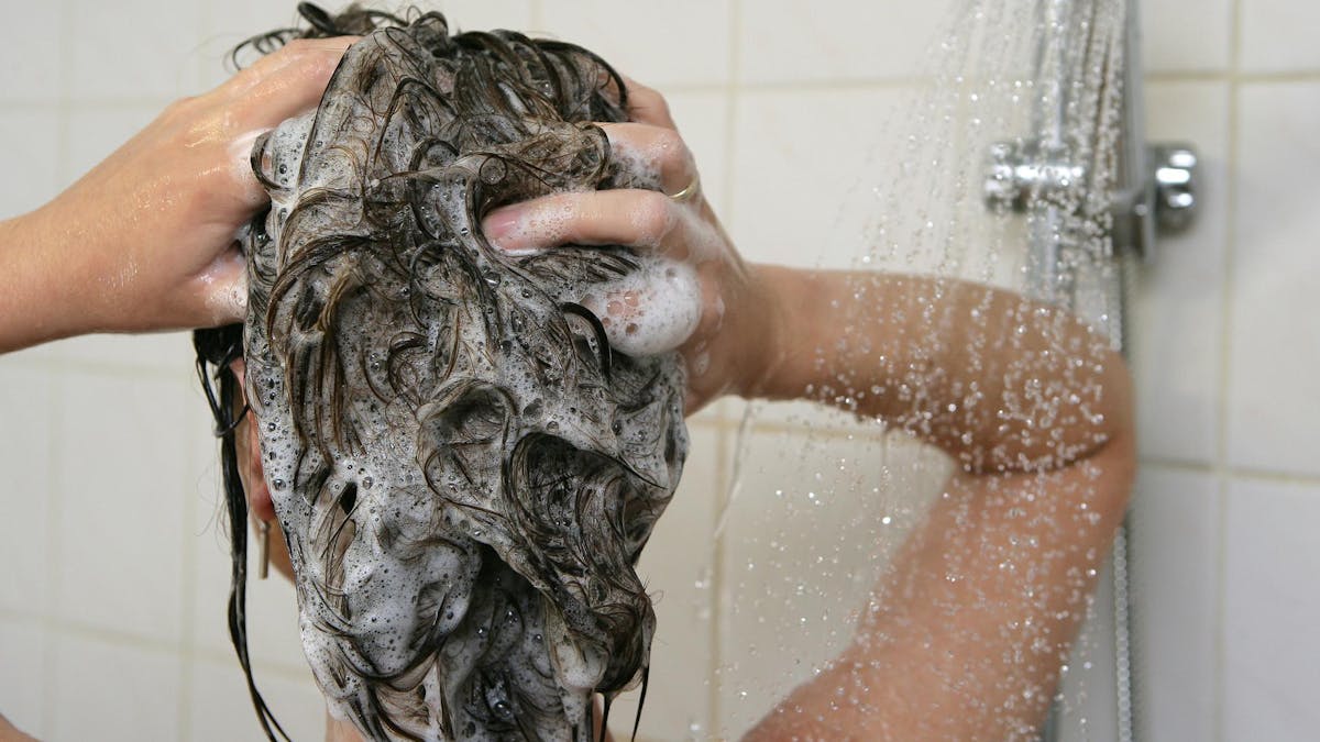 Eine Frau steht unter der Dusche und wäscht sich die Haare.&nbsp;