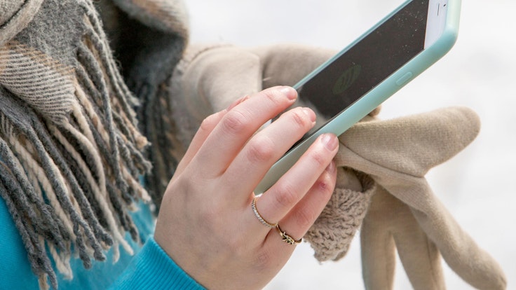 Eine Frau hält im Winter ein Handy in ihrer Hand.