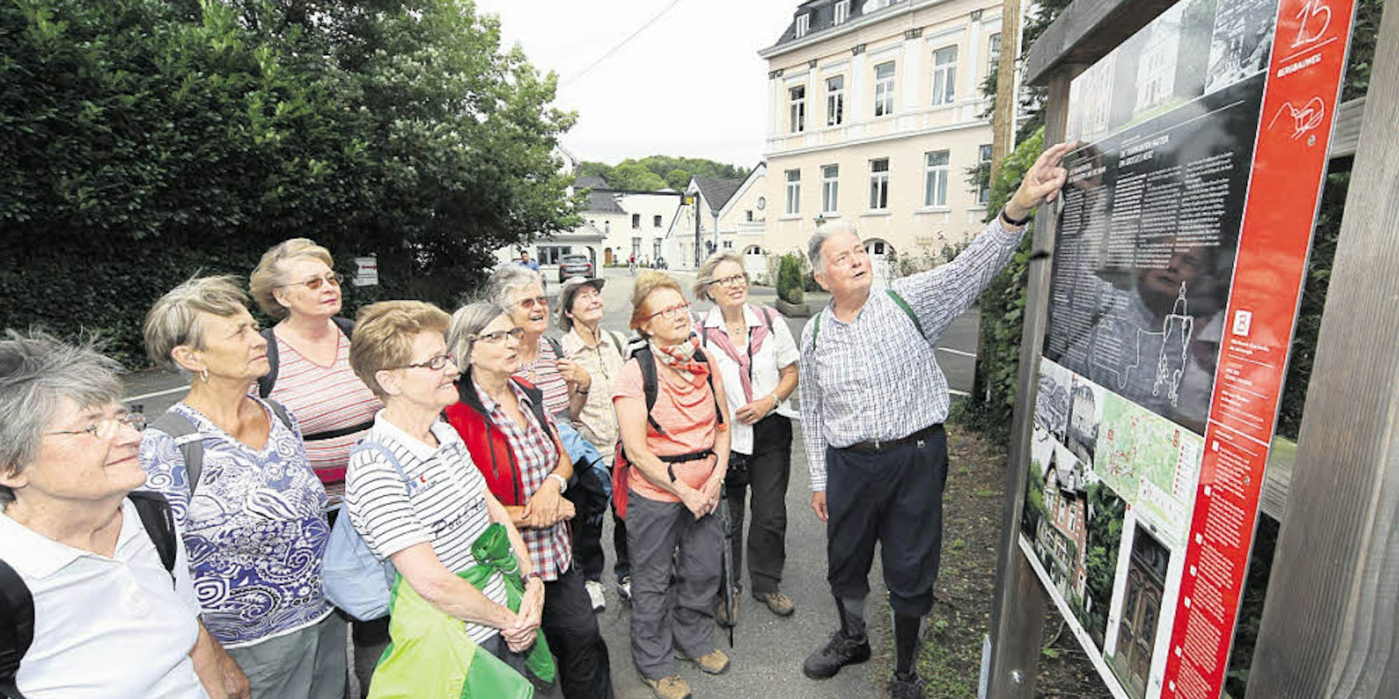 Die Geschichte des früheren Industriegeländes der Firma Reusch (im Hintergrund) erläutert Rolf Wermelskirchen seiner Kölner Wandergruppe an einer Infotafel des Bergischen Streifzugs „Bergbauweg“.