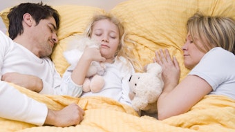 Ein etwa sechsjähriges Kind schläft zwischen seinen Eltern im Bett.