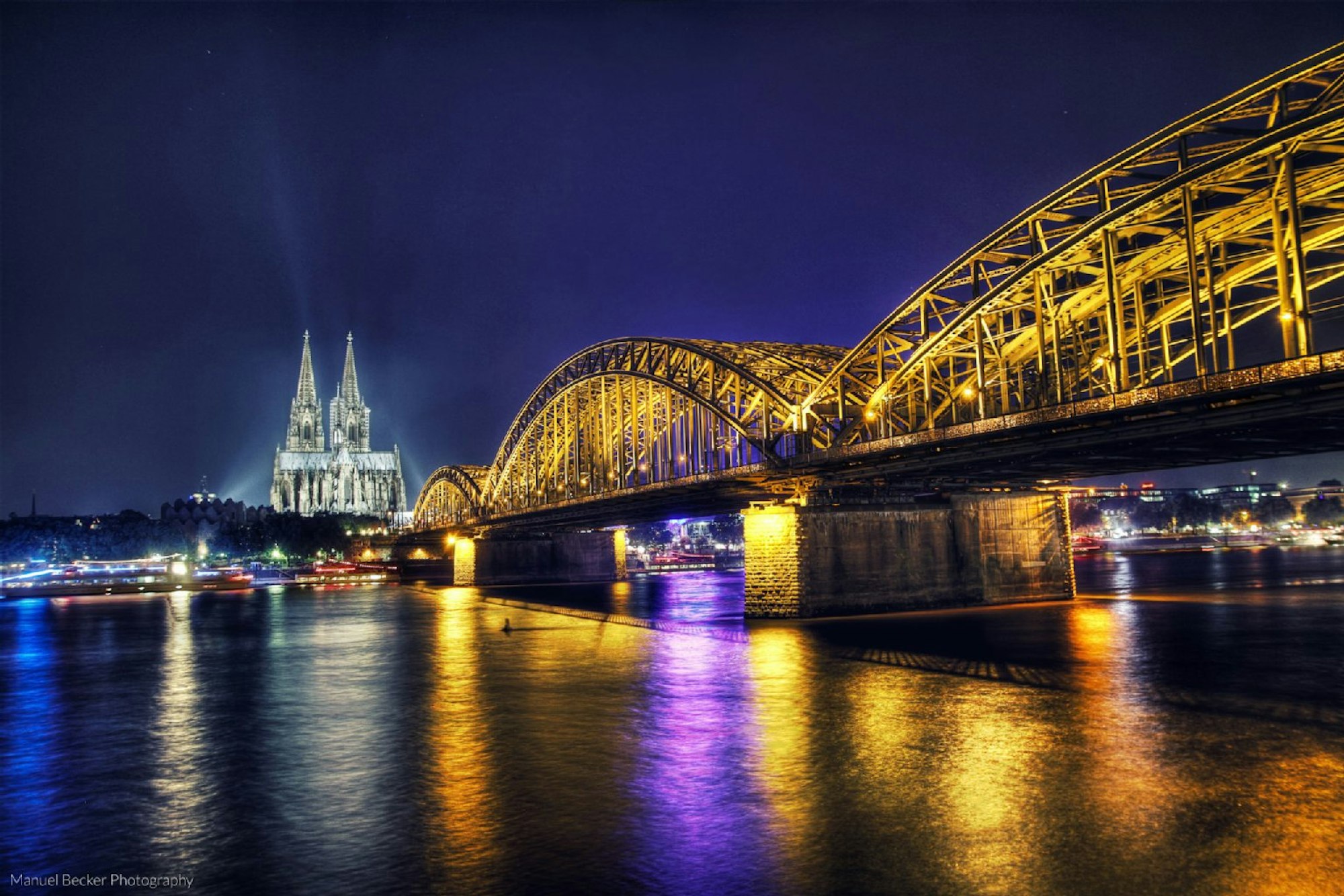 Dom und Hohenzollernbrücke werden des Nachts beleuchtet.
