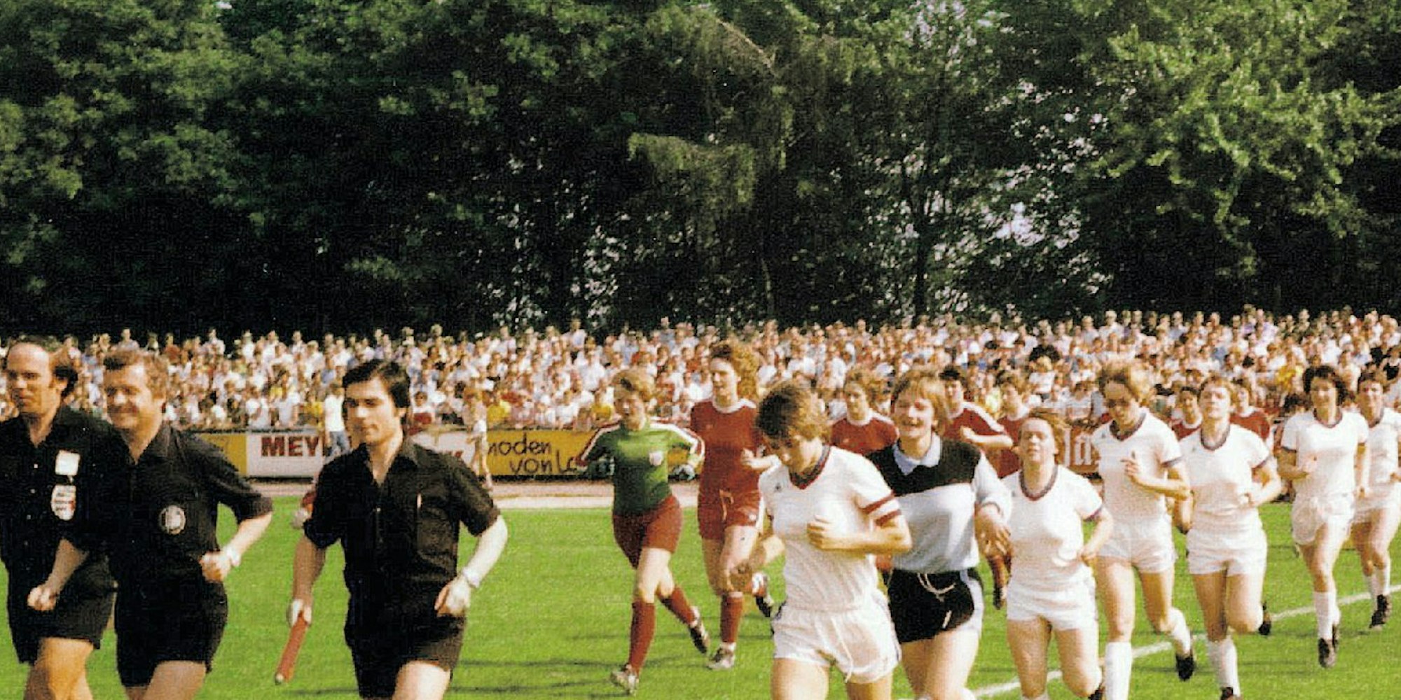 1977 vor 7840 Zuschauern im Gladbacher Stadion: Die Mannschaften von Bayern München und Bergisch Gladbach 09 laufen zum zweiten Halbfinale (4:0) ein. Vorn Spielführerin Bettina Krug, Zweite von rechts ist Irmgard Stoffels.