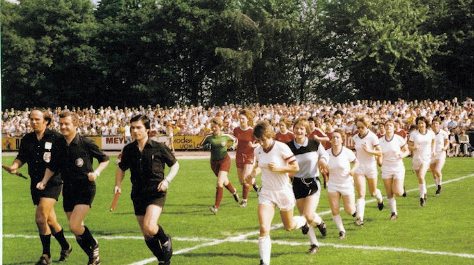 1977 vor 7840 Zuschauern im Gladbacher Stadion: Die Mannschaften von Bayern München und Bergisch Gladbach 09 laufen zum zweiten Halbfinale (4:0) ein. Vorn Spielführerin Bettina Krug, Zweite von rechts ist Irmgard Stoffels.