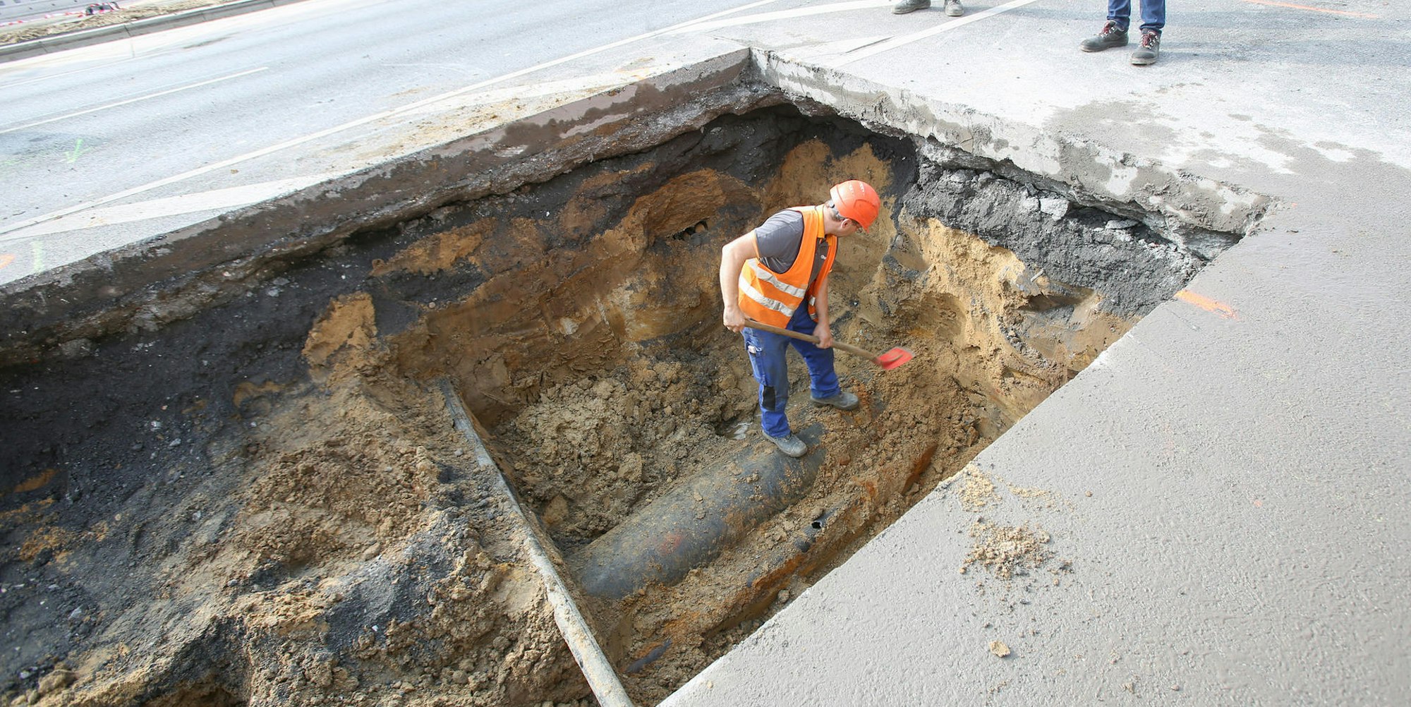 Ein Arbeiter steht mit Schaufel in einem großen Loch in der Straße.