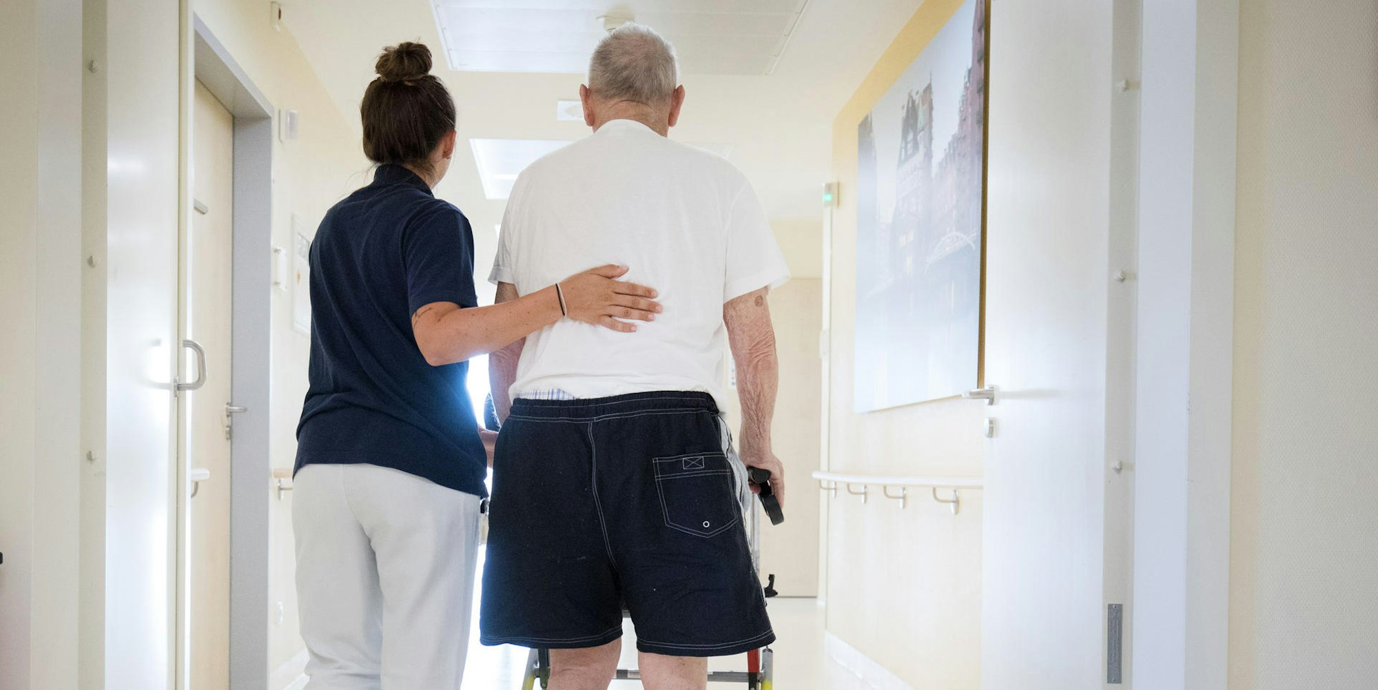 Eine Krankenschwester begleitet einen älteren Mann mit Rollator