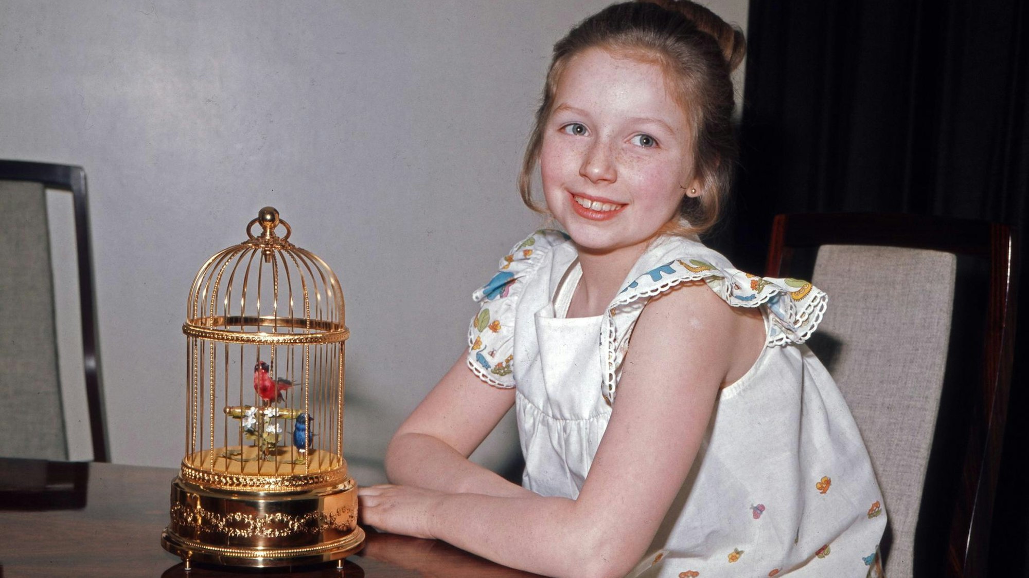Kinderstar Lena Zavaroni sitzend vor einem goldenen Vogelkäfig. Sie lacht in die Kamera.