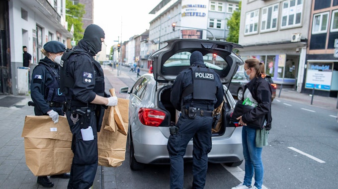 Polizisten bringen Tüten mit Beweismaterial zu einem Auto.
