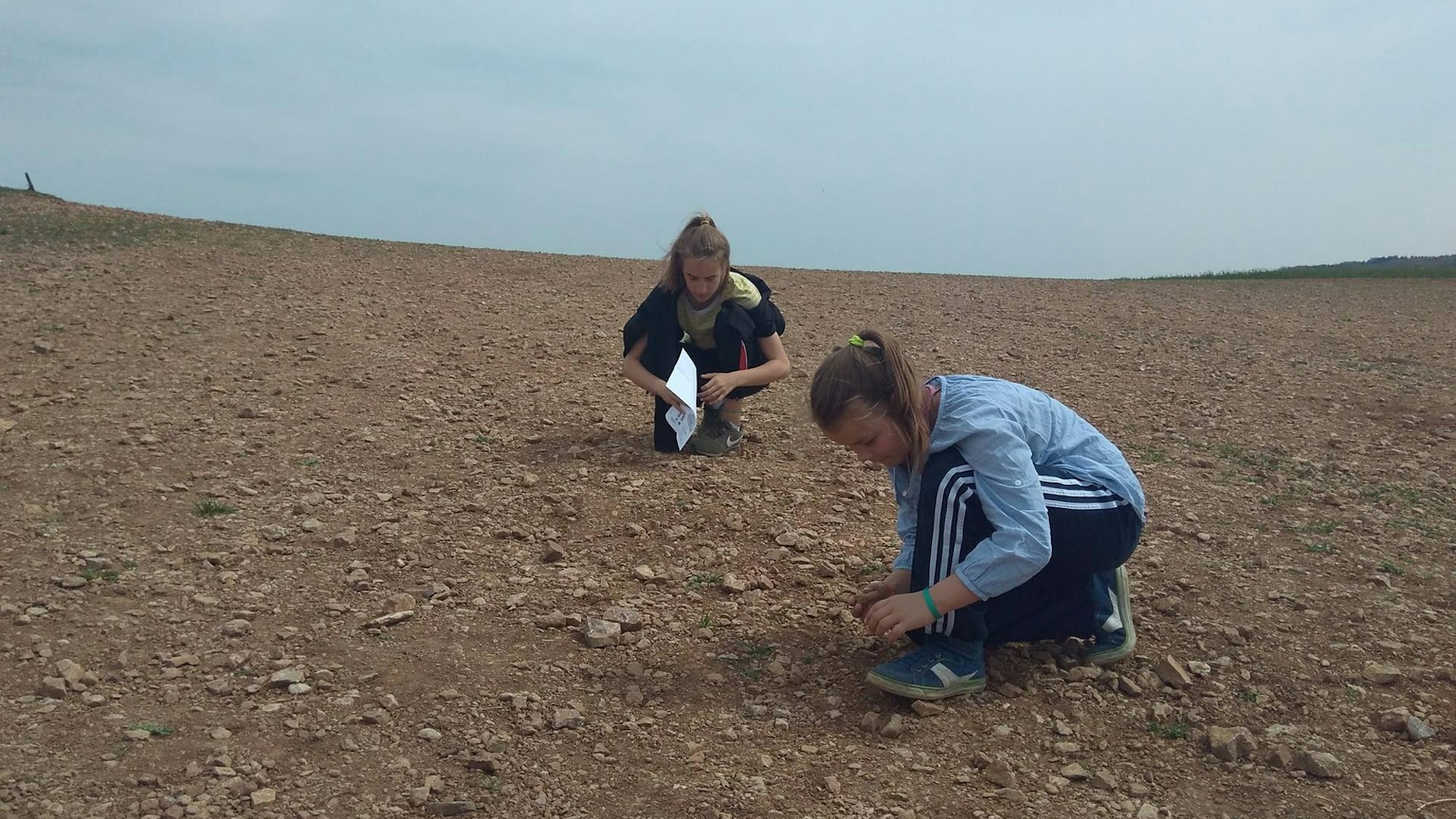 zwei Mädchen suchen auf einem Acker nach Fossilien