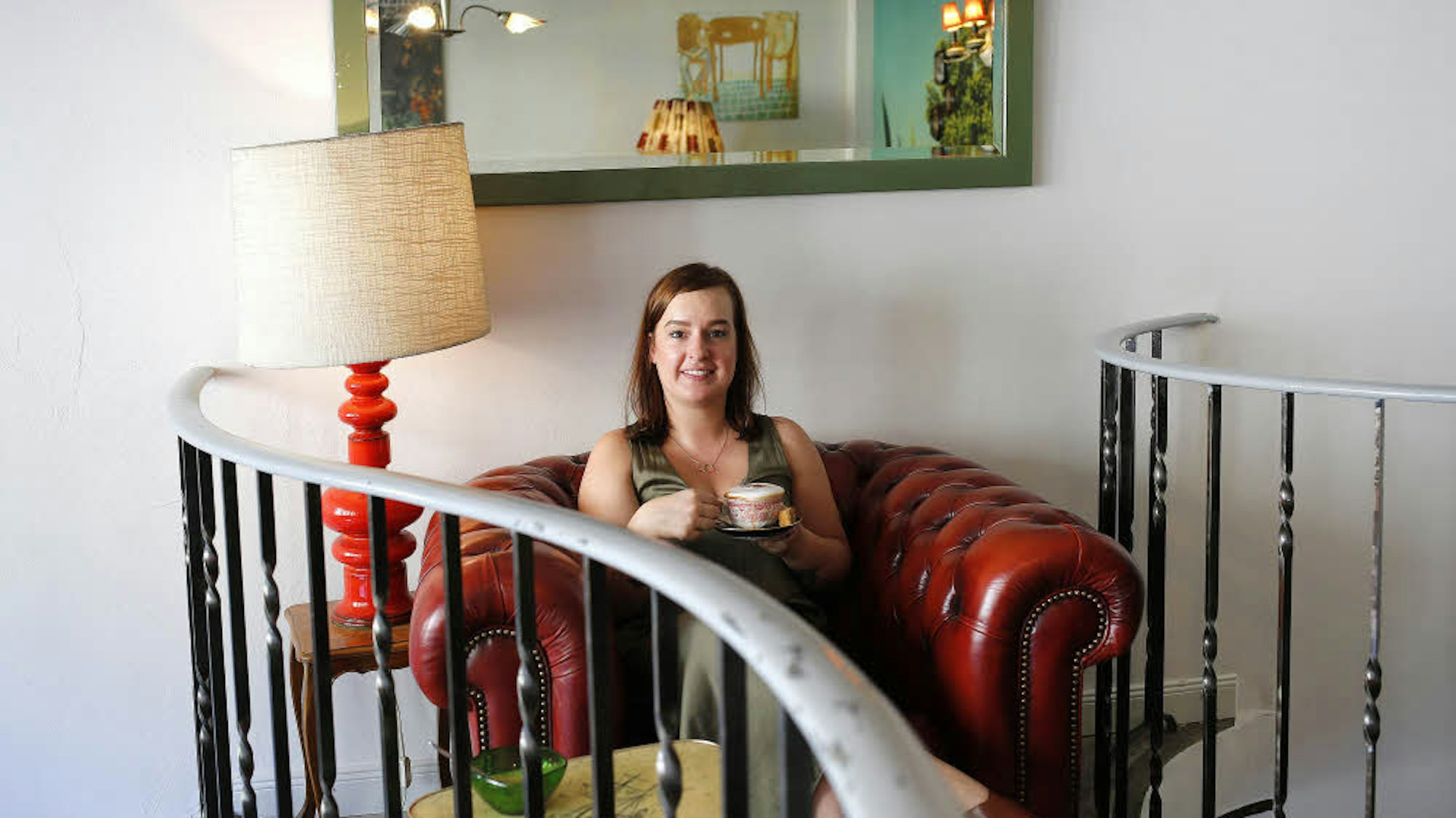 Julia Floß in der Leuchte Kaffeebar in Köln, sie sitzt in einem roten Retro-Sessel und hält eine Kaffeetasse.