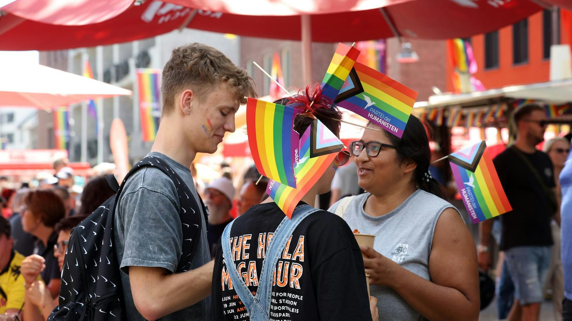 Menschen unterhalten sich beim ColognePride. Sie haben Pride-Flaggen im Haar.