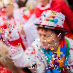 Menschen feiern Karneval in Köln und werfen Konfetti in die Luft.