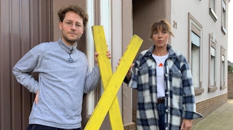 David und Marita Dresen stehen vor einem Haus und halten ein gelbes Kreuz zwischen sich.