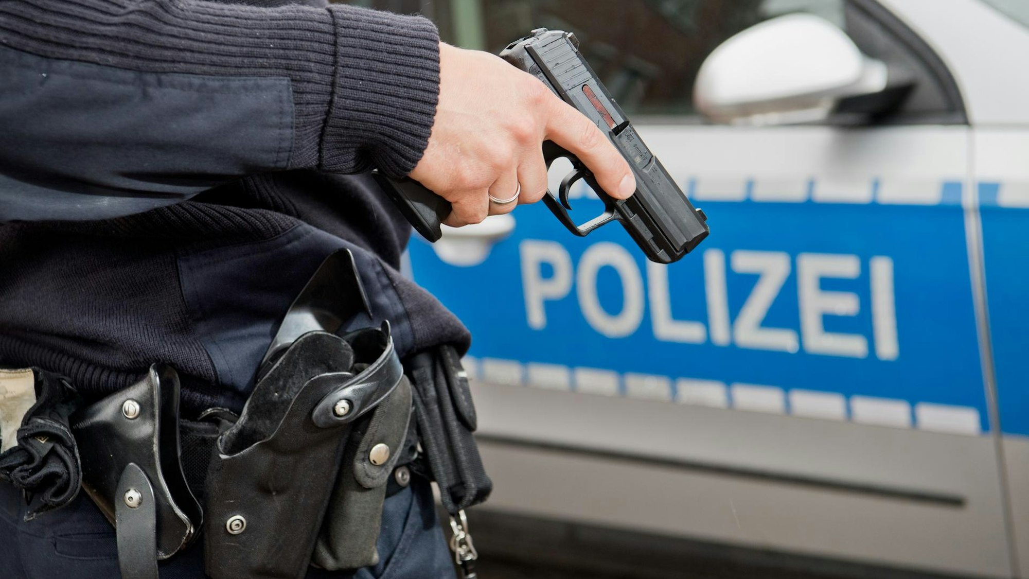 Ein Polizist steht mit gezogener Pistole vor einem Streifenwagen.