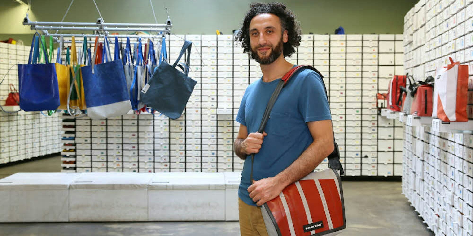 Storemanager Mohammed Darwich vor der Kartonwand mit rund 1600 Taschen.