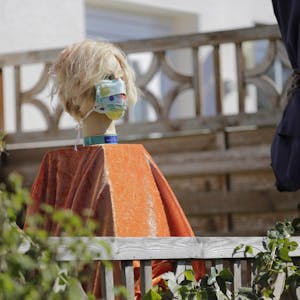 Eine Puppe mit Mundschutz am Siebenborn weist den Weg zu Haus Nummer 78, wo Sabine Häger jeden Tag eine Box mit selbstgenähten Masken aufstellt.