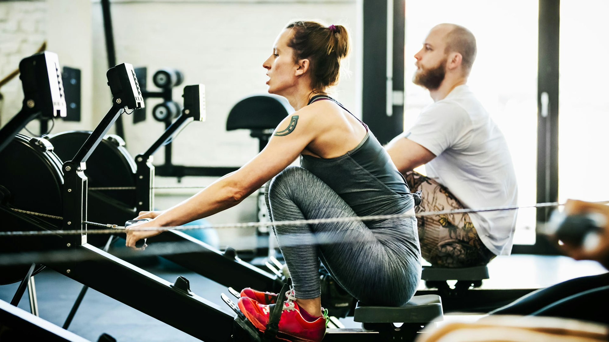 Eine Frau und ein Mann trainieren an einer Rudermaschine im Fitnessstudio.