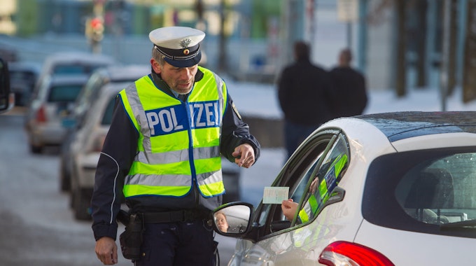 Ein Polizist steht bei einer Kontrolle neben einem Auto.