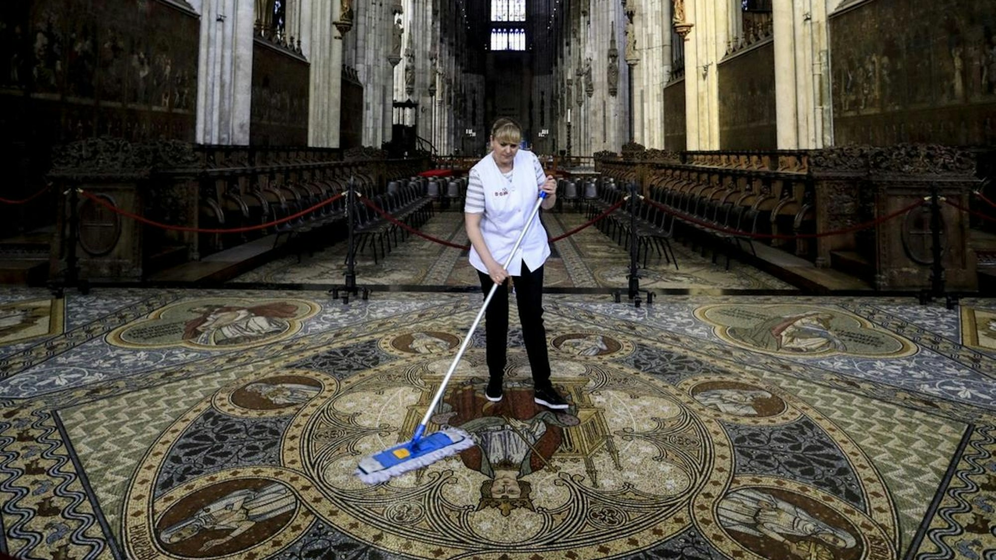 Eine Reinigungskraft wischt das Mosaik zwischen Chorgestühl und Dreikönigenschrein.