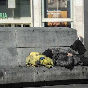 Ein Obdachloser liegt auf einer Bank.
