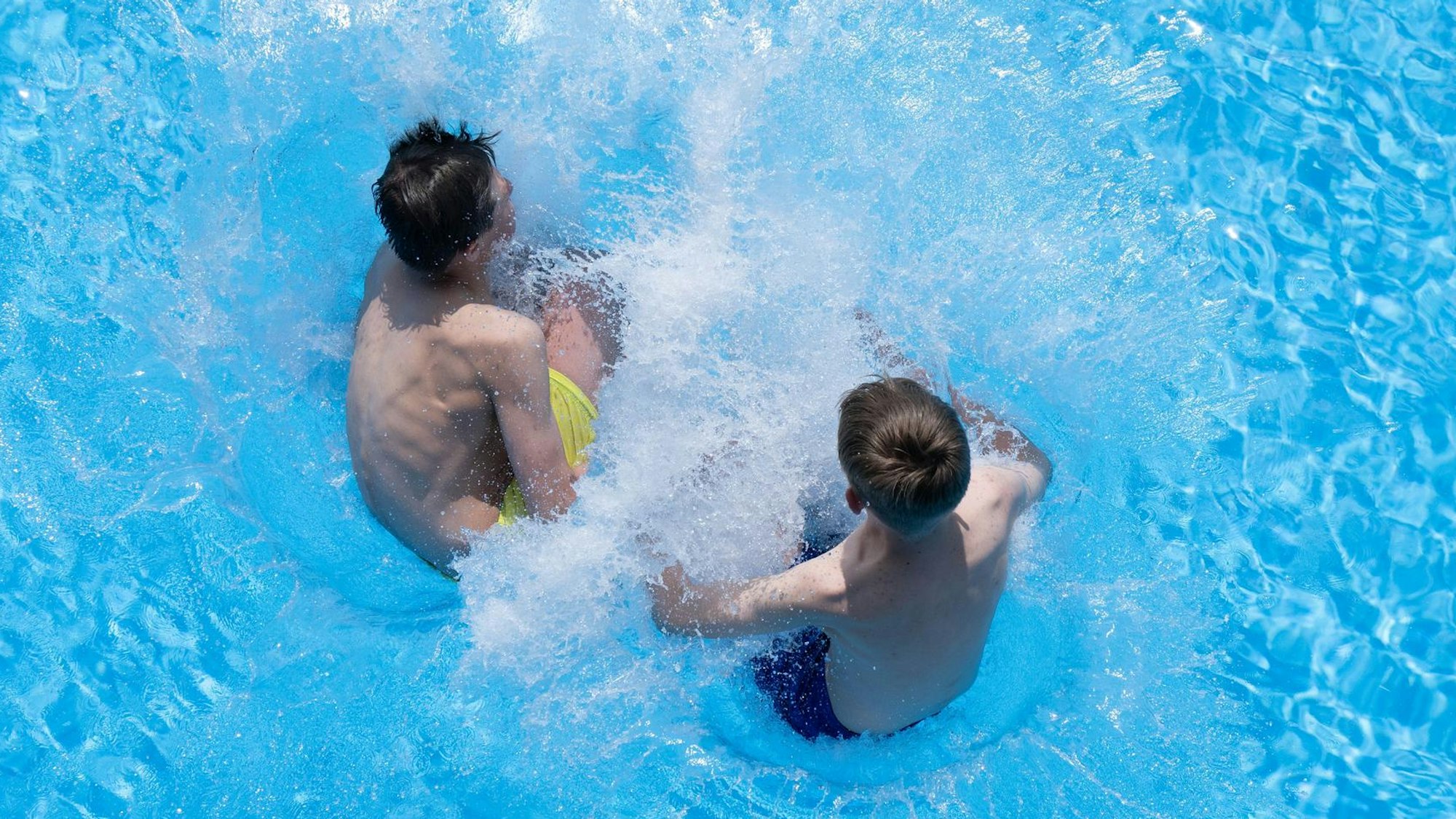Zwei Jungs springen i einem Freibad ins Wasser.
