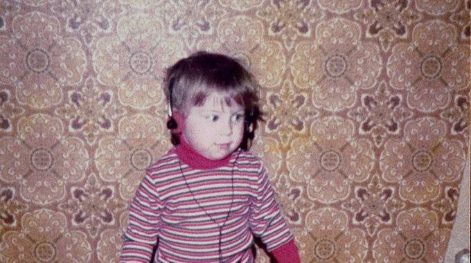 Kerstin Ott als Kind im bunt gestreiften Pullover, mit einem Kopfhörer auf der wuscheligen Frisur, der zugehörige Walkman baumelt an den Beinen.