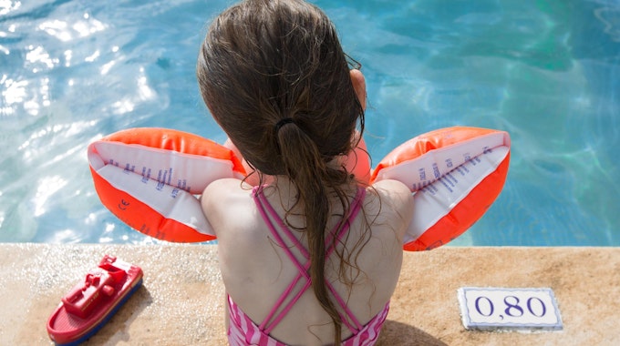 Ein Mädchen sitzt mit Schwimmflügeln am Beckenrand.