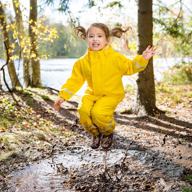 Kind in gelber Regenkleidung springt im Matsch