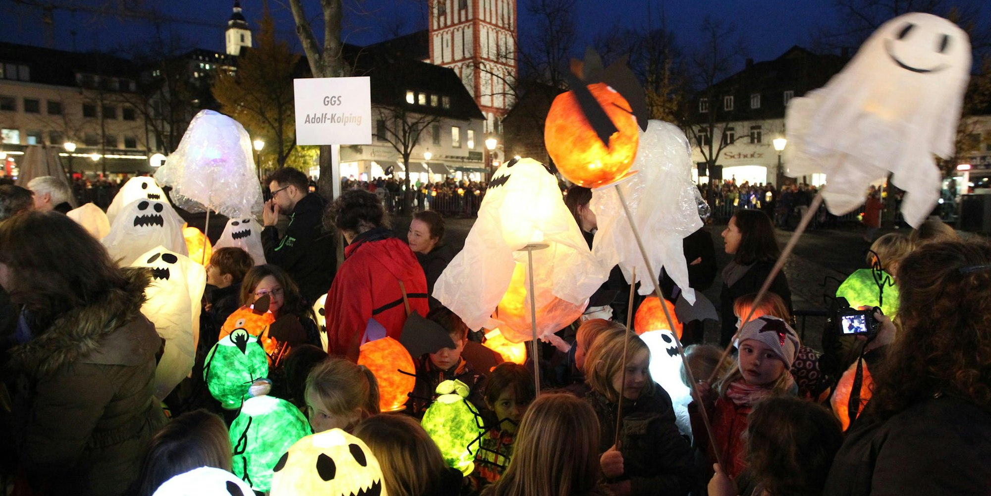 Auf dem Siegburger Marktplatz stehen viele Kinder mit ihren Laternen, die aussehen wie Geister.