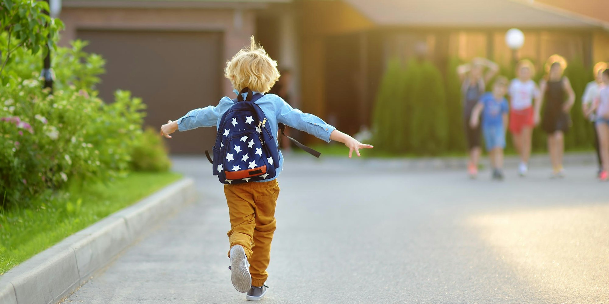 Ein Kind mit Rucksack rennt fröhlich zu anderen Kindern.