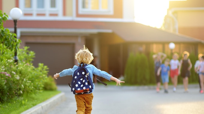 Ein Kind mit Rucksack rennt fröhlich zu anderen Kindern.