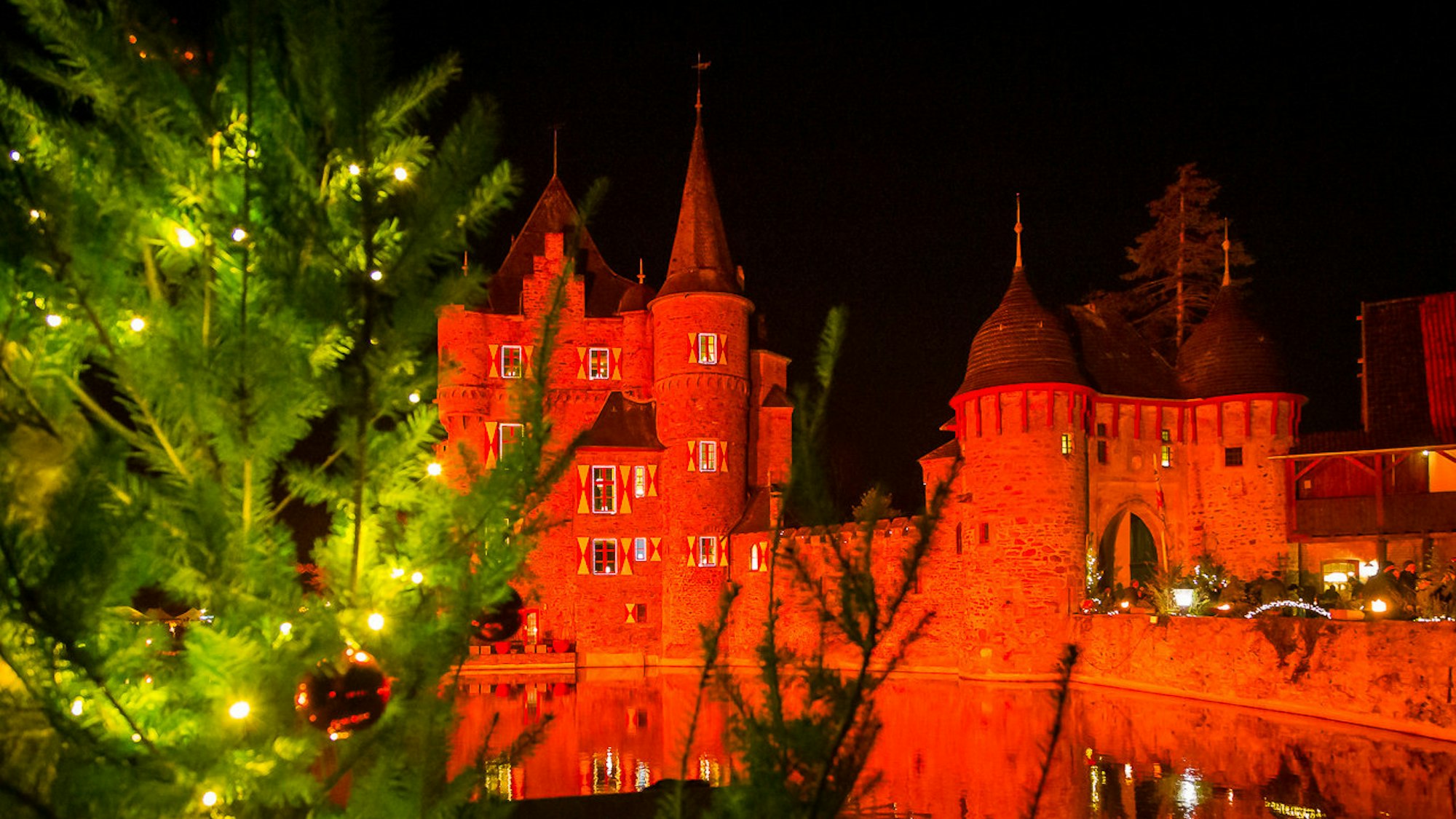 Rot angestrahlte Burg mit Tannenbaum im Vordergrund