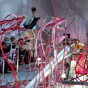 Knäuel aus mit roter Flüssigkeit gefüllten Schläuchen umgeben die Cellistin Valerie Fritz bei „Nuqta – The beginning“.