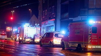 Einsatzfahrzeuge von Feuerwehr und Rettungsdienst (Notarzt- und Rettungswagen) stehen in der Nacht vor einer Häuserzeile.
