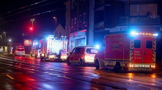 Einsatzfahrzeuge von Feuerwehr und Rettungsdienst (Notarzt- und Rettungswagen) stehen in der Nacht vor einer Häuserzeile.