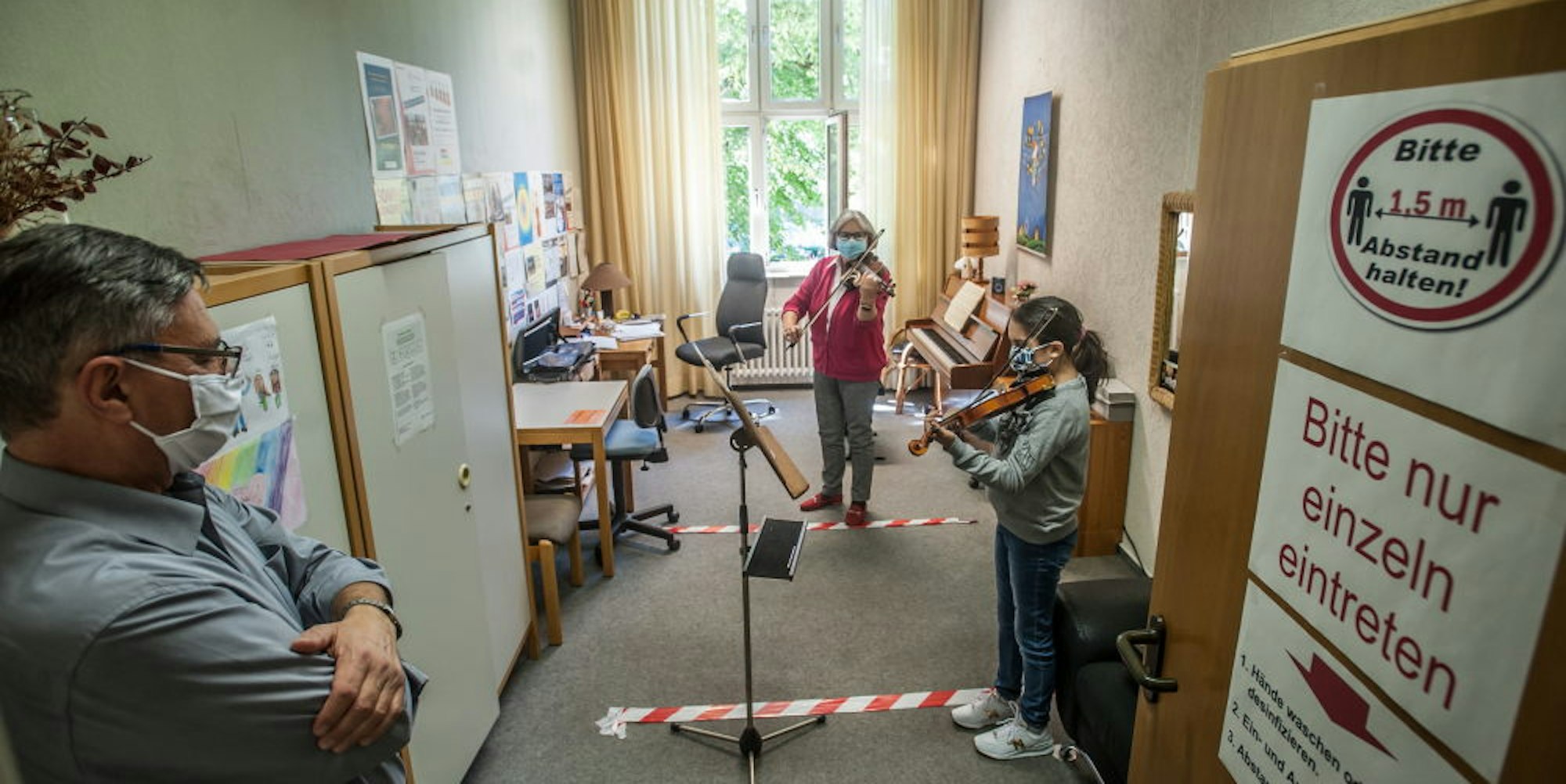 Auf Abstand: Musikschulleiter Jürgen Ohrem schaut einer Schülerin und Lehrerin Eva Messias beim Einzelunterricht zu.