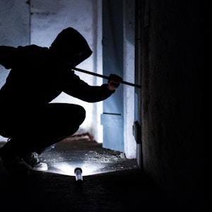 Ein Einbrecher bricht mit einer Brechstange eine Kellertür auf.