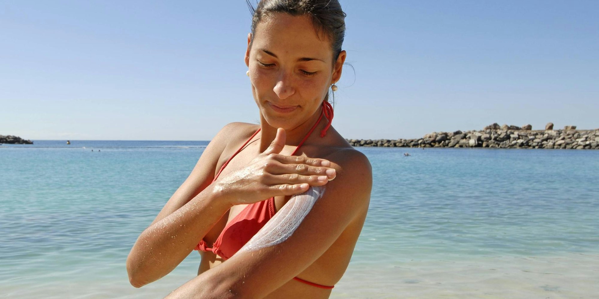 Frau cremt sich am Strand mit Sonnencreme ein