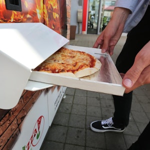 Ein Mann hält einen halbgeöffneten Pizzakarton in Händen.