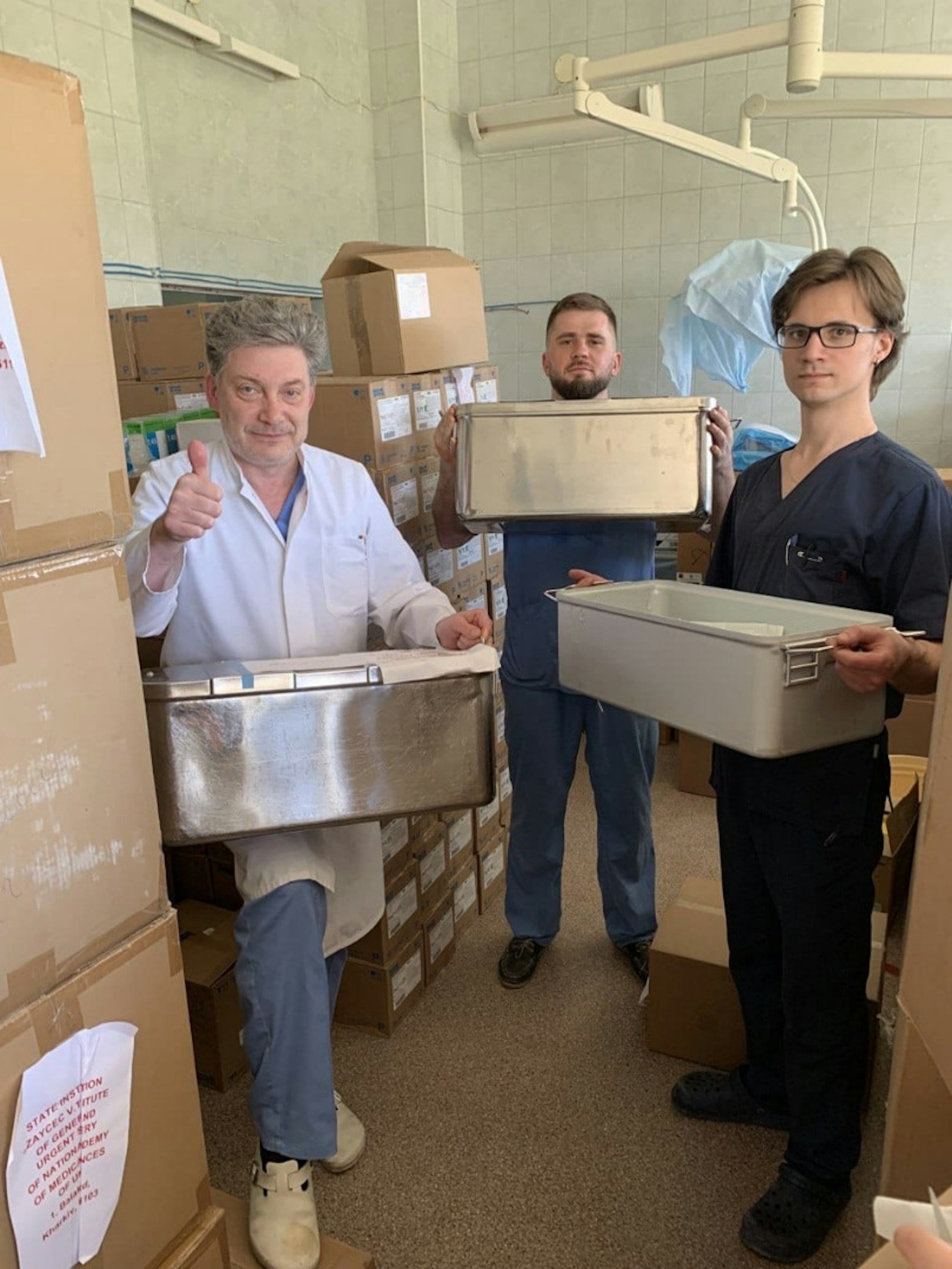 Über eine neue Medikamenten-Lieferung aus Oberberg freuen sich Dr. Vitaliy P. und sein Team, die inmitten der Stapel der neuen Kisten stehen.