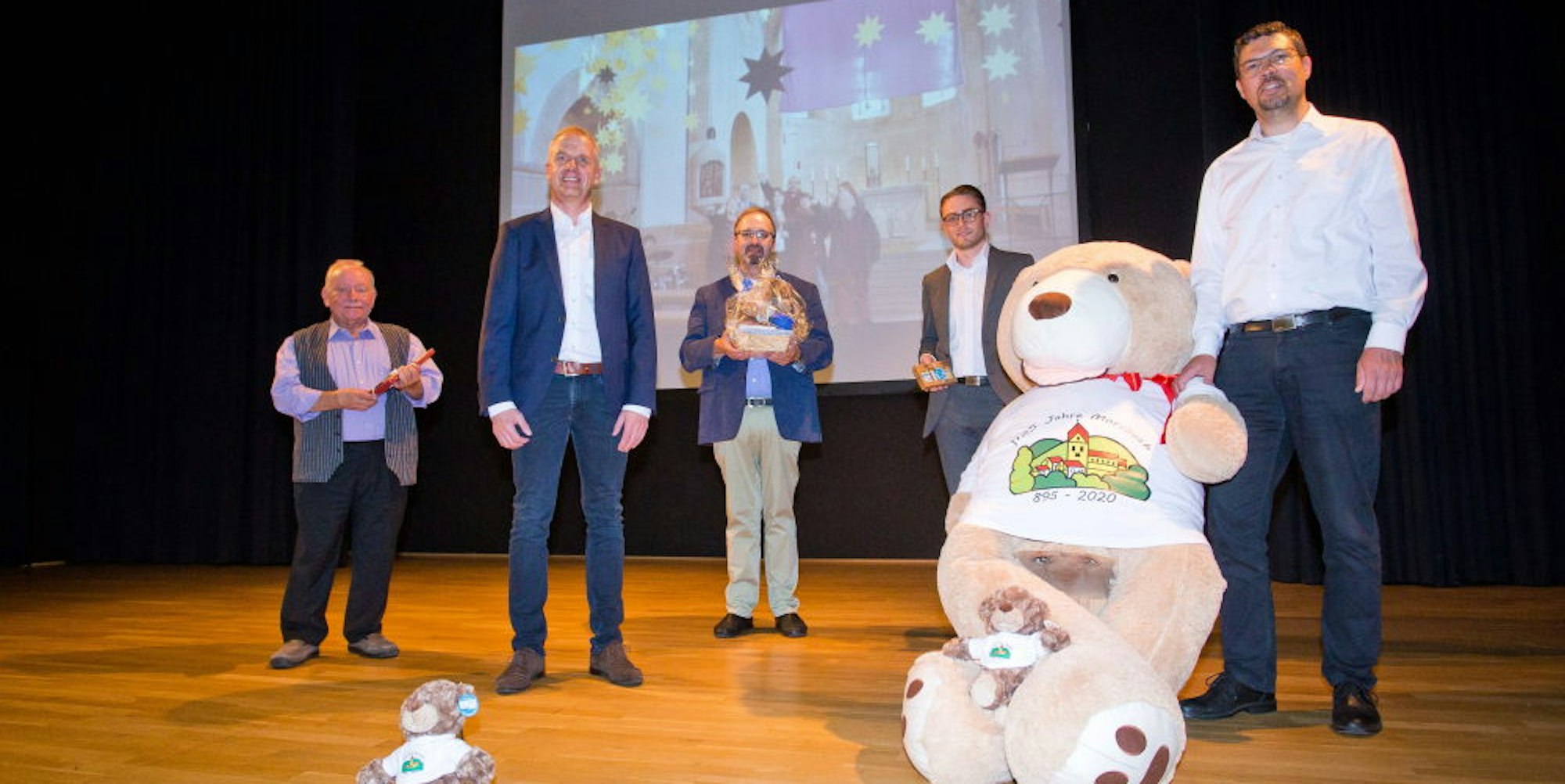 Der Morsbär spielt eine zentrale Rolle in der Übertragung am Samstag, die Bürgermeister Jörg Bukowski (r.) nun vorgestellt hat.