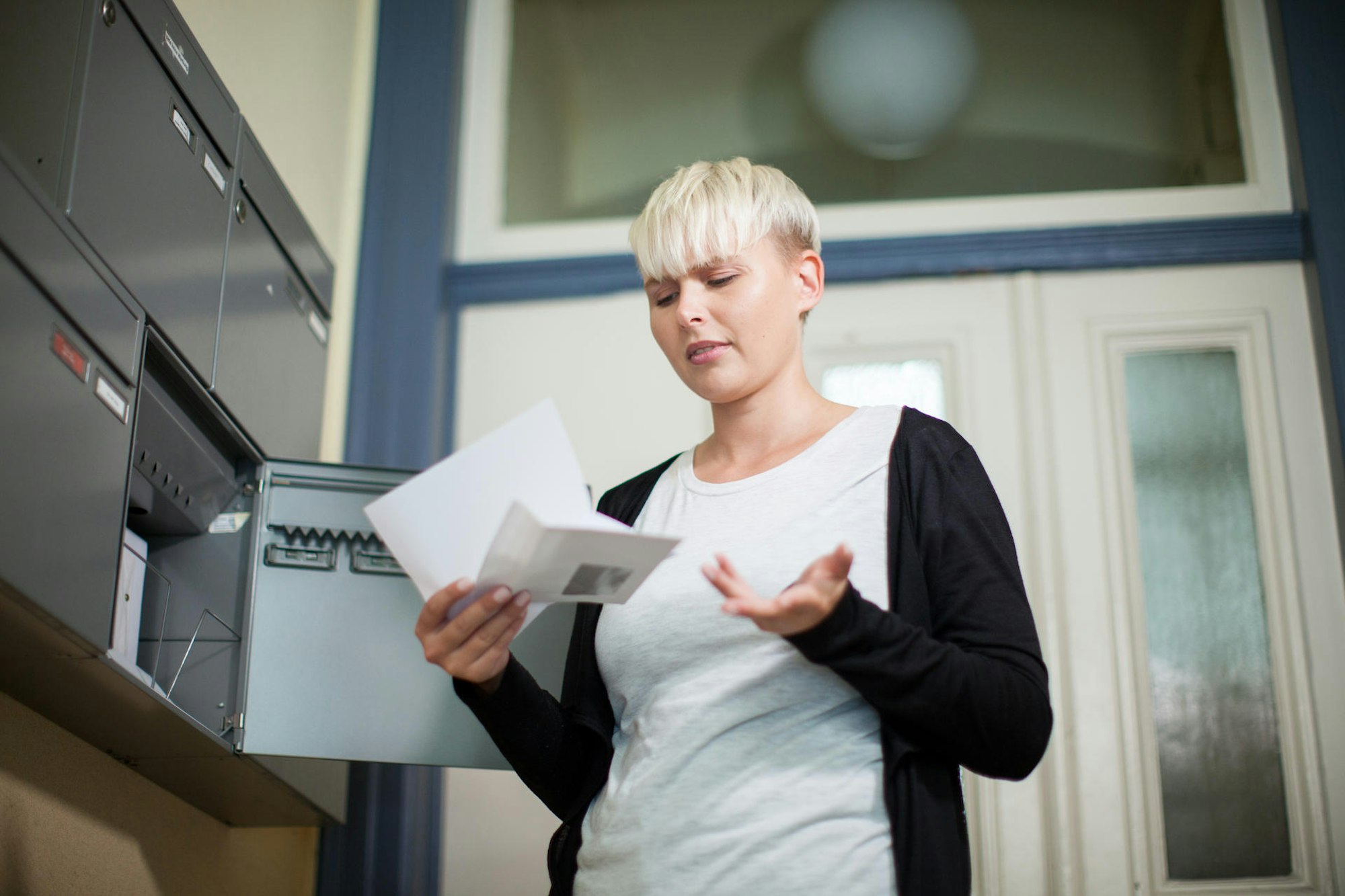 Eine Frau steht mit einem Brief in der Hand vor einem Briefkasten.